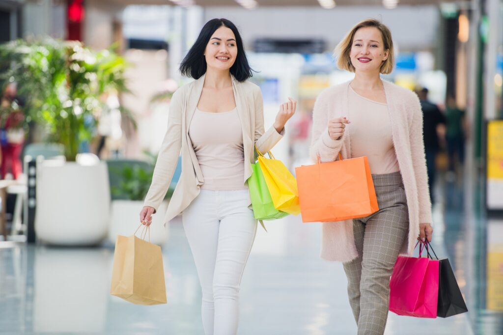 Two happy young women walking in shopping mall with shopping bags